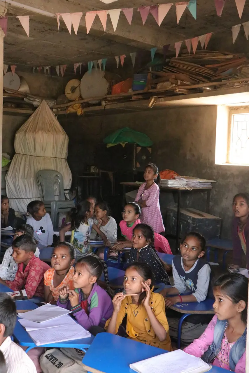 Children at their desks in a village classroom, looking up towards the front of the room