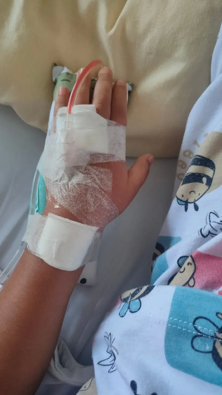 A child's hand resting on a hospital bed with an intravenous line taped in place