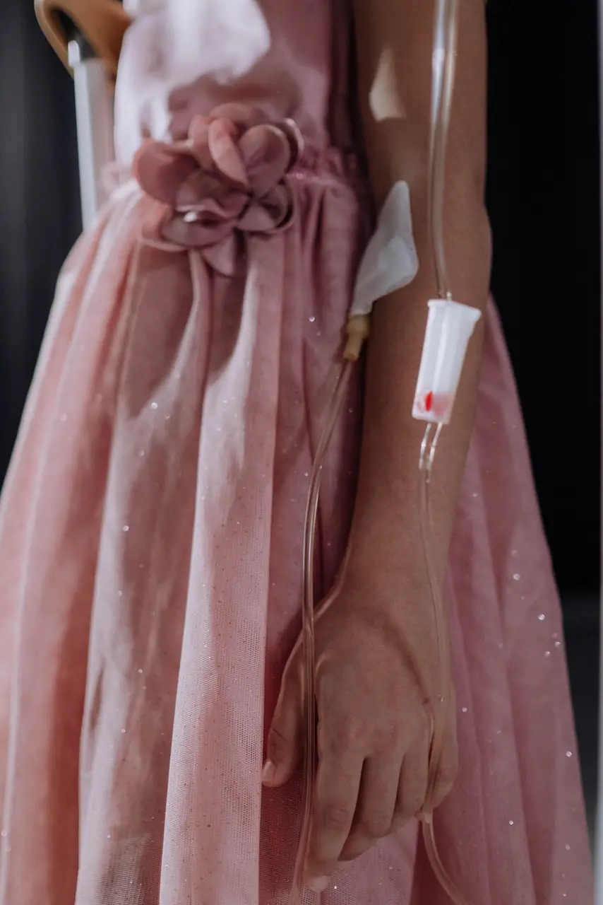 A young girl in a pink dress standing beside an IV stand during treatment